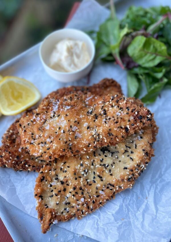 Chicken Schnitzel with Sesame Seeds on a tray with lemon wedges, salad and mayo