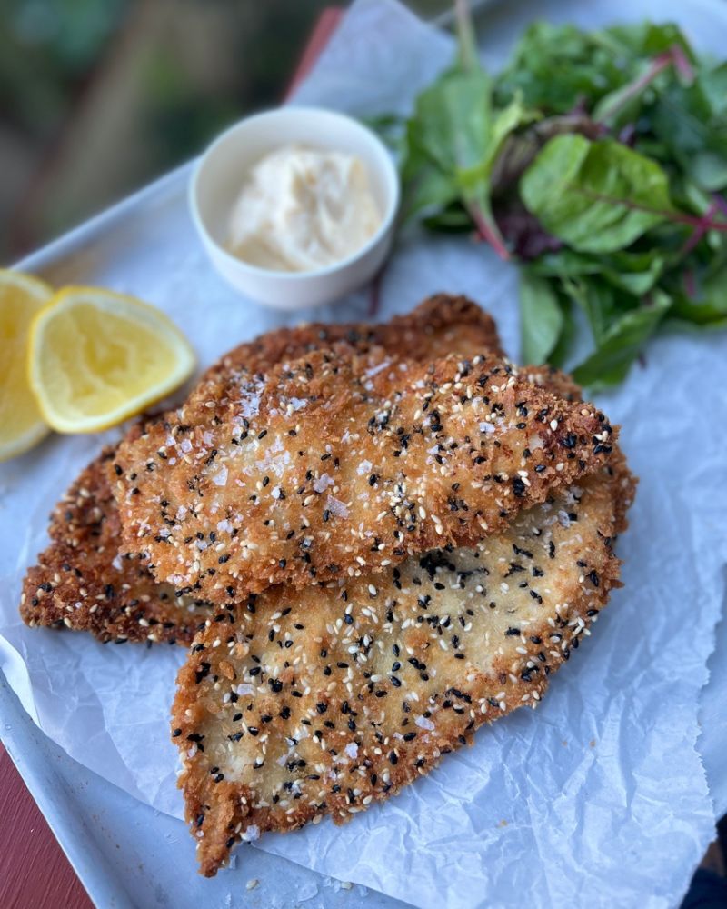 Crispy Chicken Schnitzel with Sesame Seeds on a tray with lemon wedges, salad and mayo