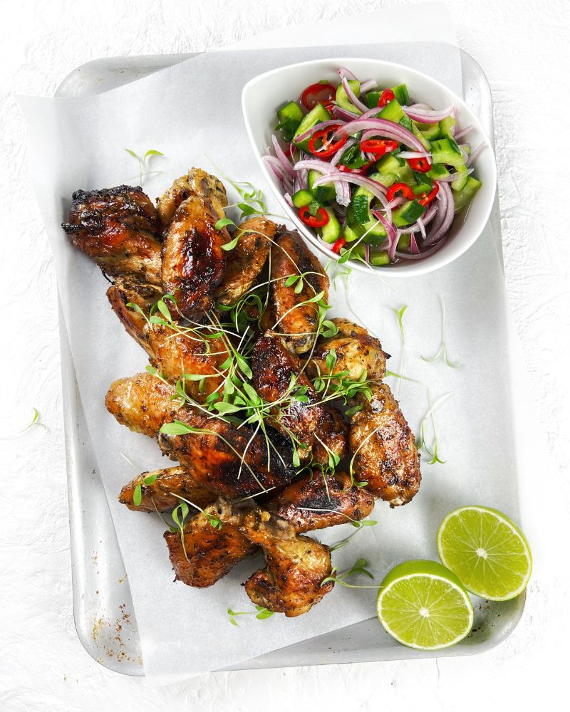 Chicken wings on a tray with lime halves and bowl of cucumber salad