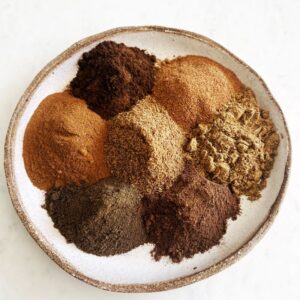 7 spices piled onto a plate on white background