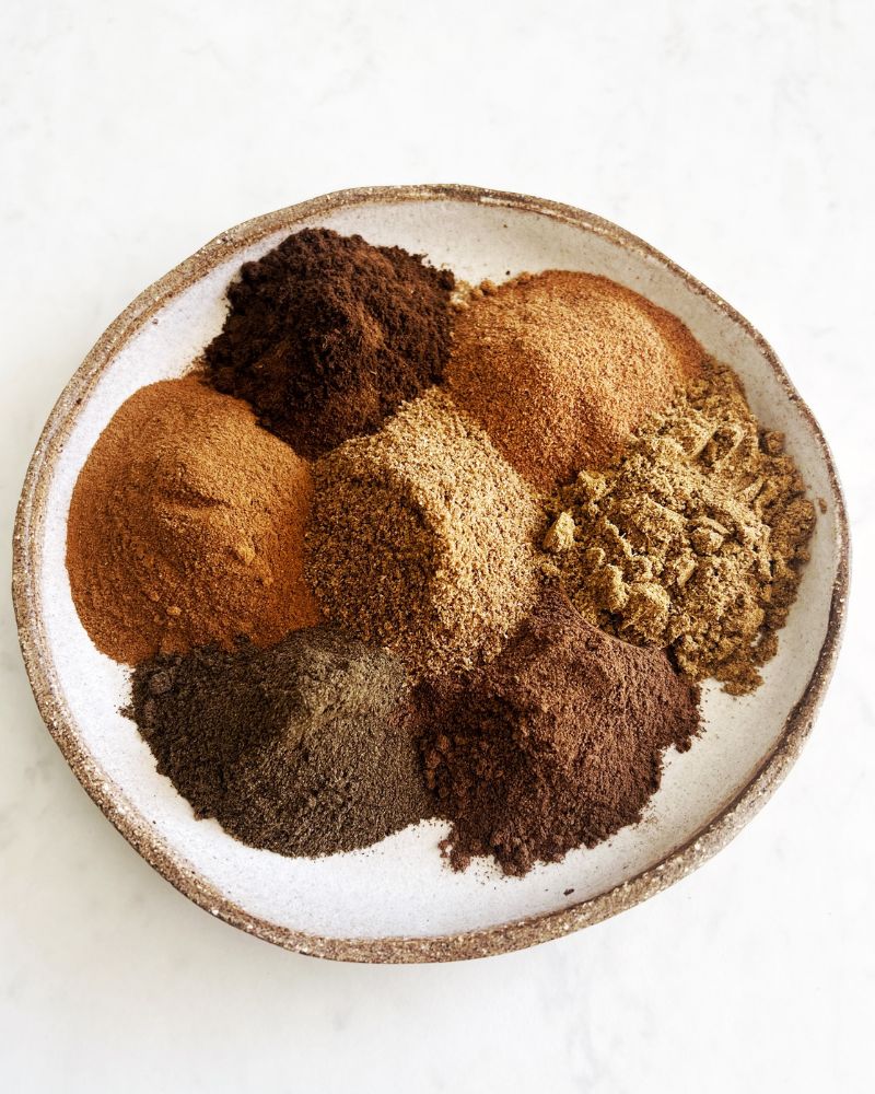 7 spices piled onto a plate on white background