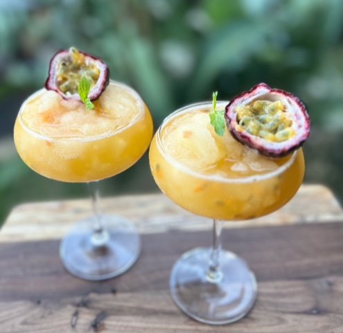 frozen frosty pash cocktails served in glasses on a board with passionfruit half as a garnish