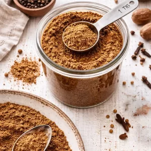 glass jar filled with 7 spice and spoon in it. spices around the outside.