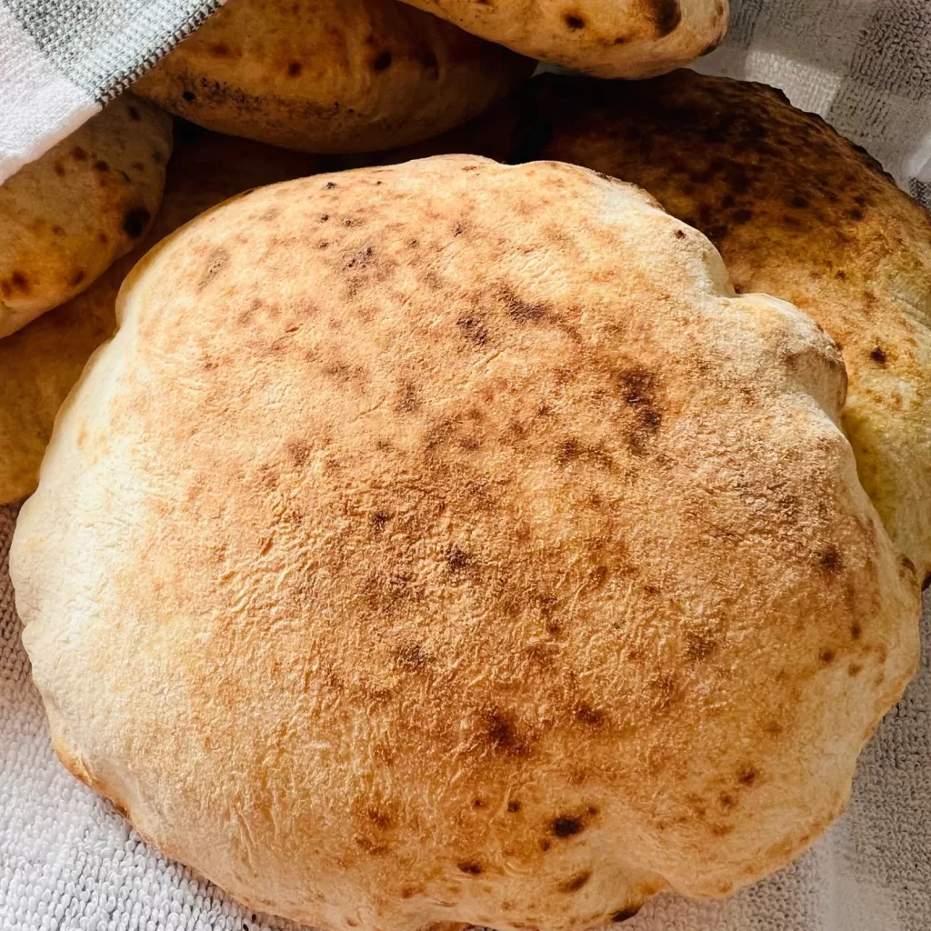 Close-up of freshly baked homemade pita bread with golden blistered surface under a tea towel.