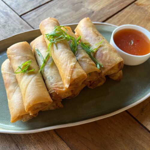 CHICKEN AND HAM SPRING ROLLS ON PLATE with sweet and sour sauce and garnished with spring onions