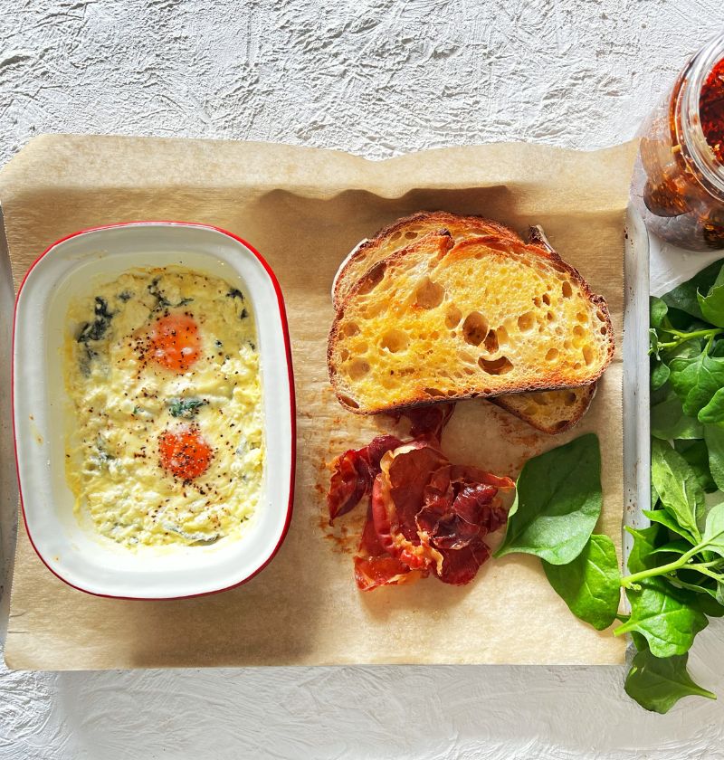 BAKED EGGS ON TRAY WITH TOAST, SAUCE AND GREENS