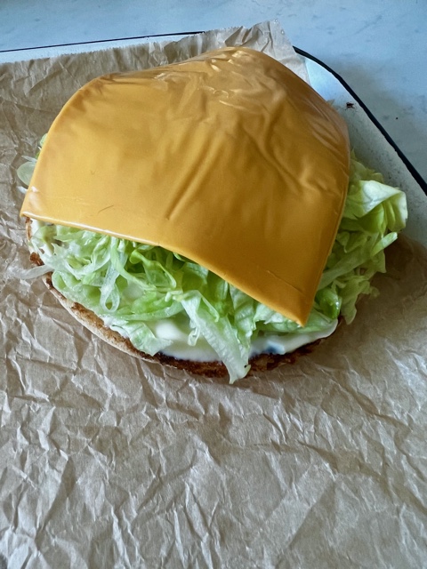 burger bun topped with mayonnaise, lettuce and cheese on a lined baking tray