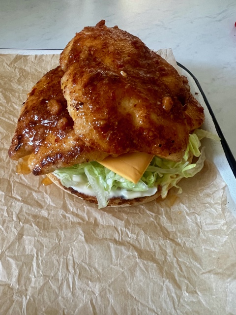 burger bun topped with mayonnaise, lettuce, cheese and peri peri chicken slices on a lined baking tray