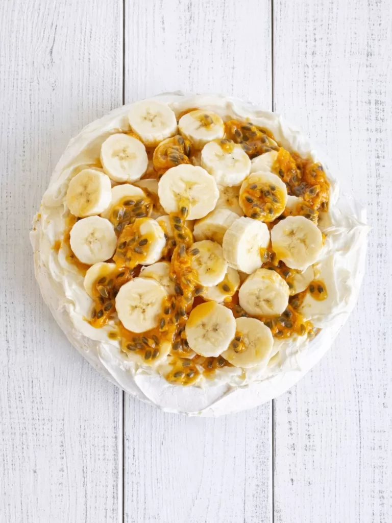 pavlova topped with banana and passionfruit pulp on white timber background