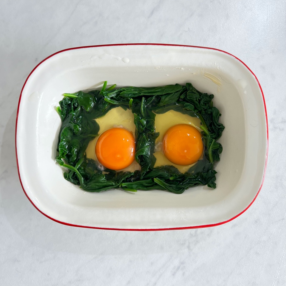 spinach in a ramekin in a figure 8 with 2 eggs cracked in it. ready to be baked