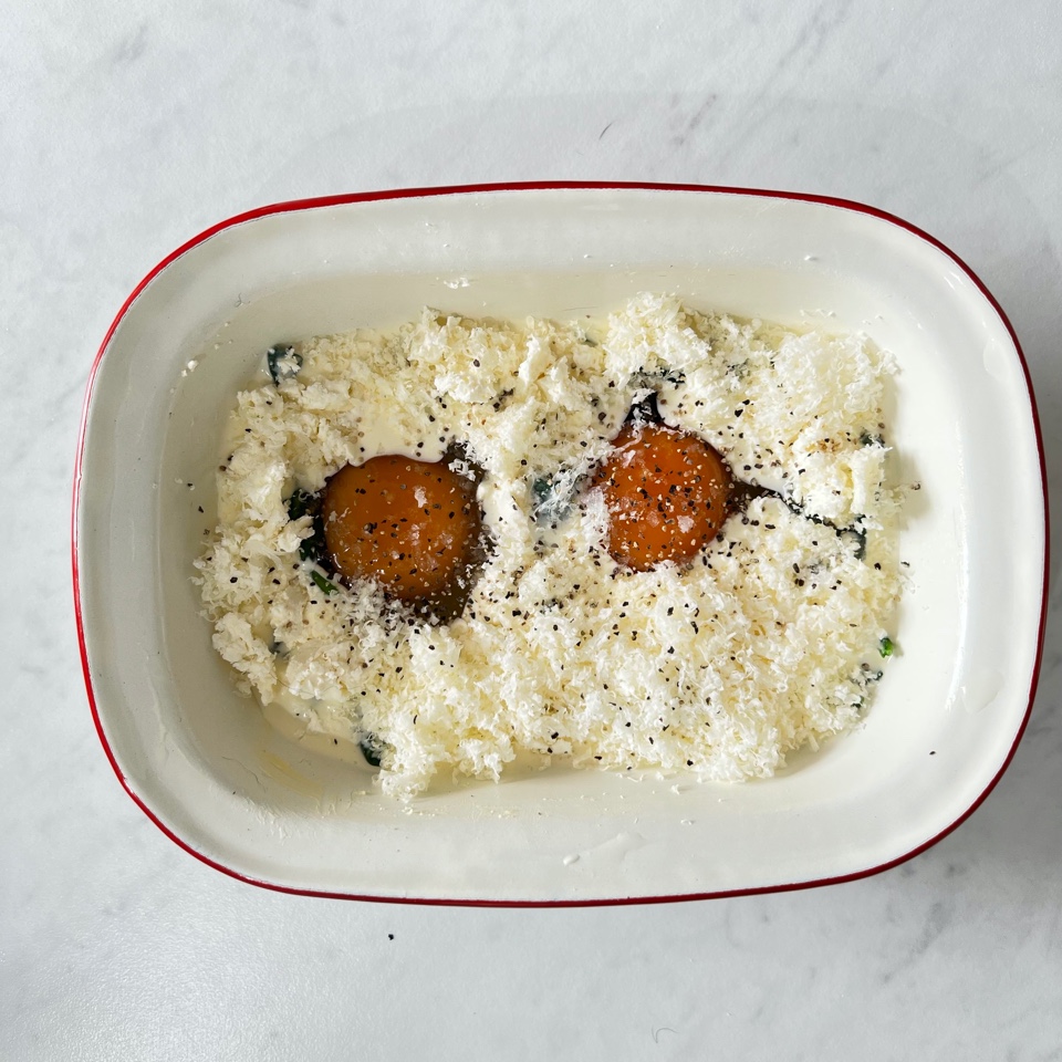 2 eggs in a ramekin with cream, feta and parmesan. Ready to be baked