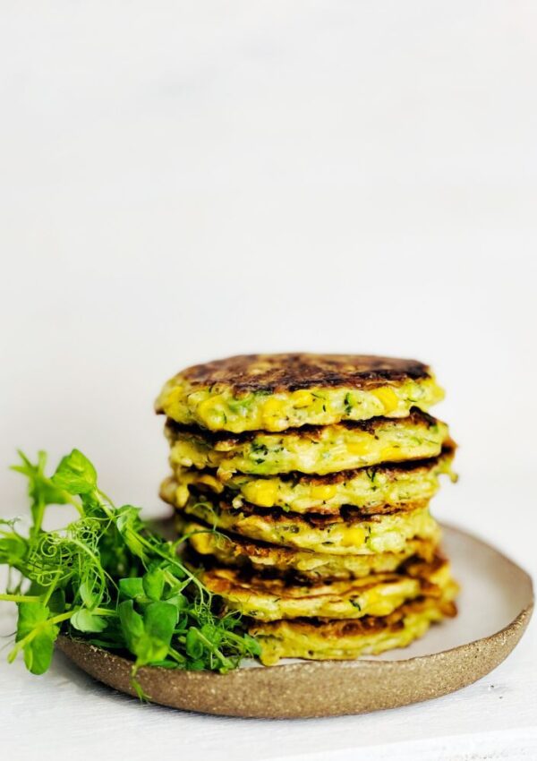 Zucchini & Sweet Corn Fritters stacked on a plate with snow pea sprouts. White background