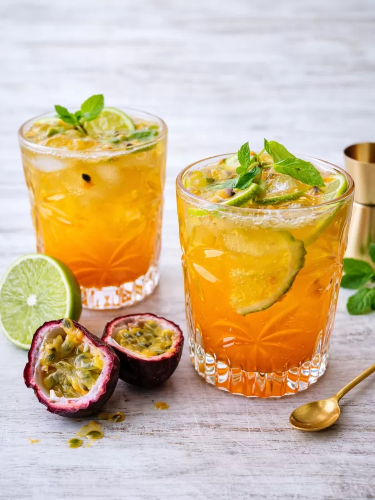 Passionfruit caipiroska with fresh lime and mint served over ice in short glasses on a white timber surface, garnished with halved passionfruit and natural light.
