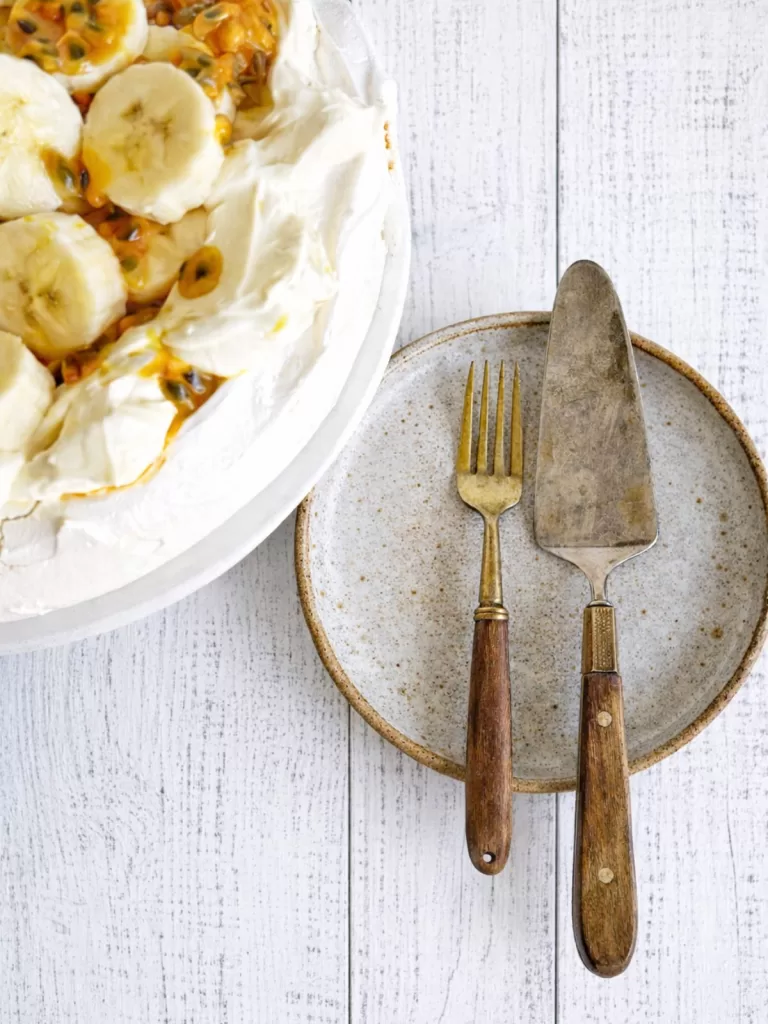 Pavlova on a white stand with a white plate next to it with a fork and cake server ready to be served