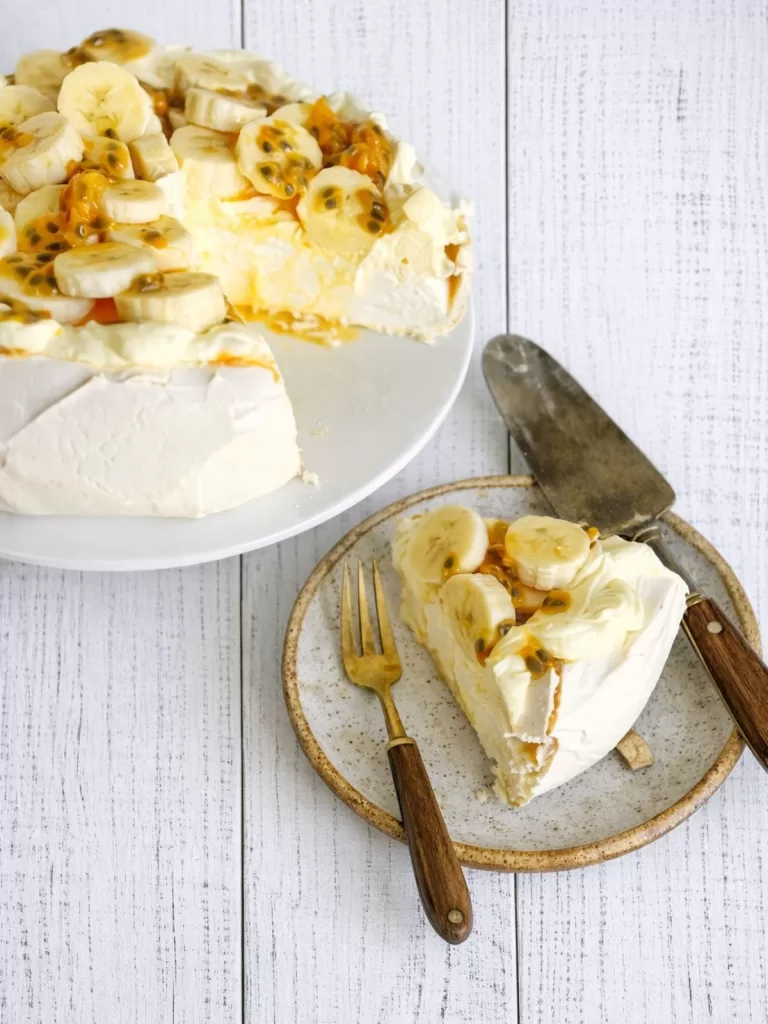 Sliced pavlova with whipped cream, banana and passionfruit pulp.