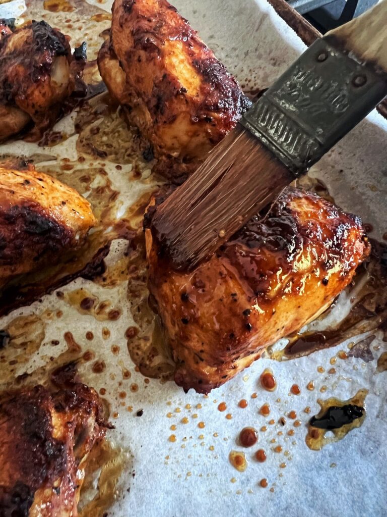 Brushing excess cooking liquid over chicken pieces with a pastry brush