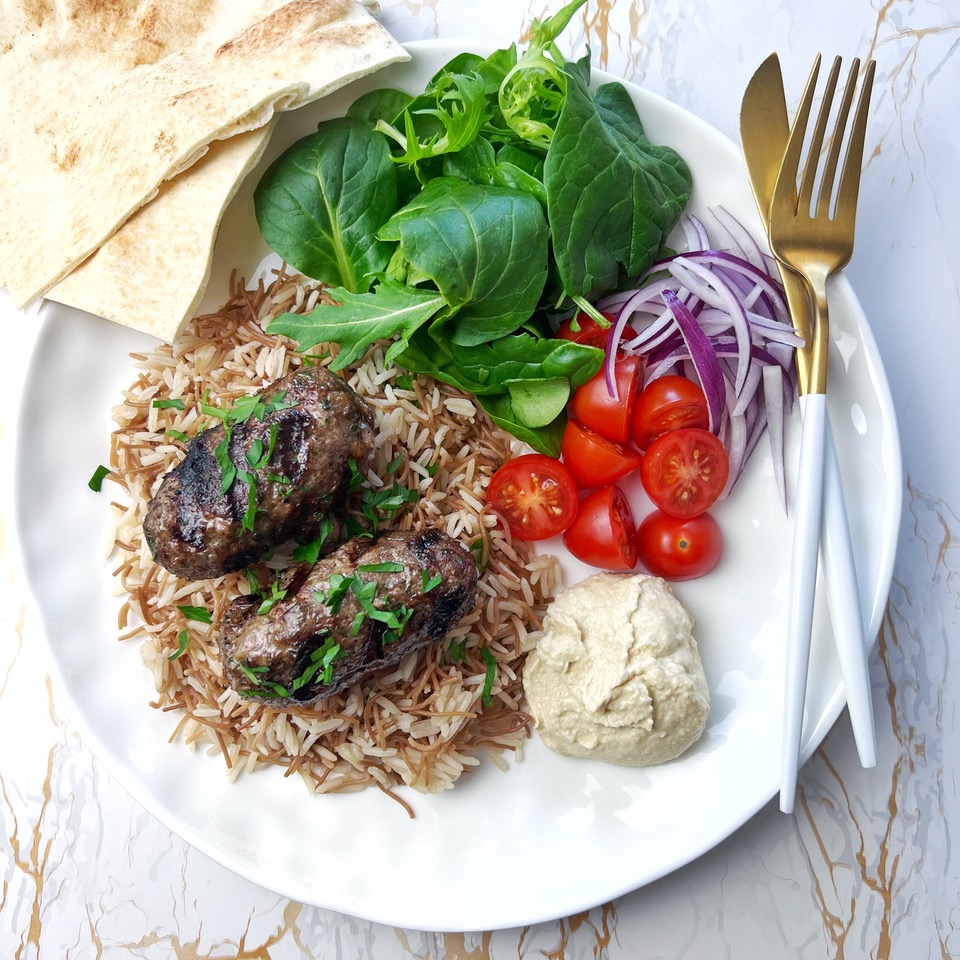 2 Lamb Kofta (Kafta) on Lebanese rice with salad on a white plate with Bread and cutlery