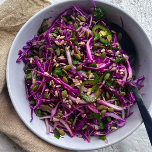 red cabbage salad in a white bowl with black spoon on a beige napkin