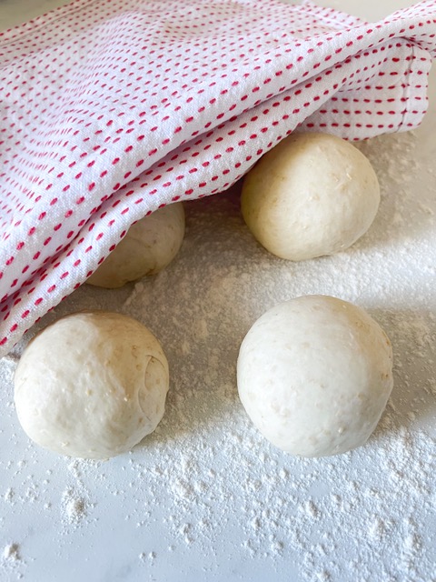 Pita bread rolled inot balls on a floured surface wtih tea towel over them