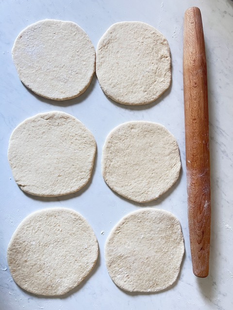Pita bread rolled out. There is 6 of them with a rolling pin laying next to them on a floured surface