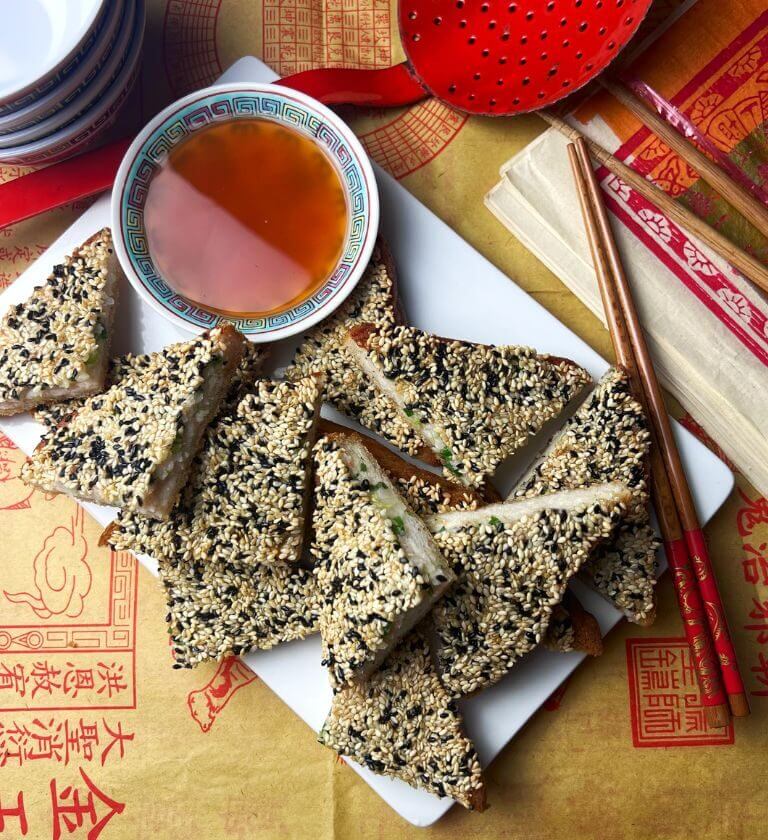 Prawn toast triangles with sweet & sour sauce on Chinese paper background with chopsticks & bowls