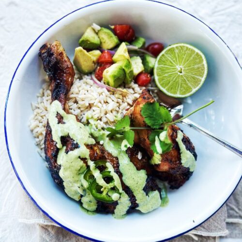 Peruvian Chicken with Green Sauce in a bowl with rice and avocado salsa and lime half