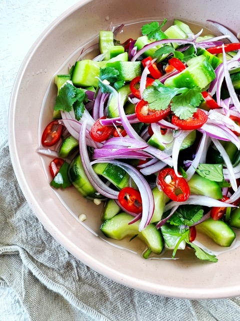 Pickled cucumbers in pink bowl on white background