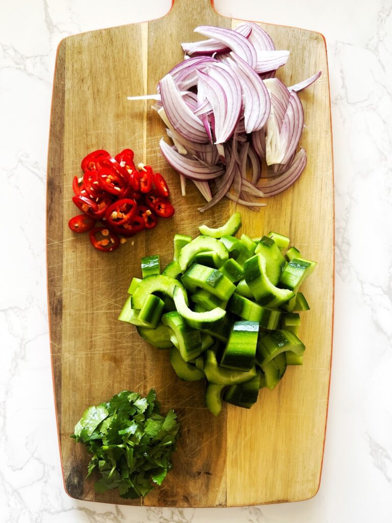 chopping board with onion, chilli, cucumber and coriander in piles for the quick pickled asian cucumbers