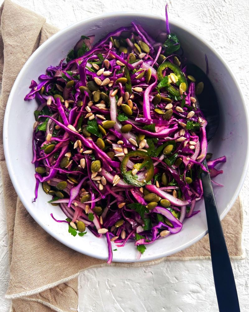 Red Cabbage Salad with Honey Lime Dressing in a bowl with spoon on a tea towel