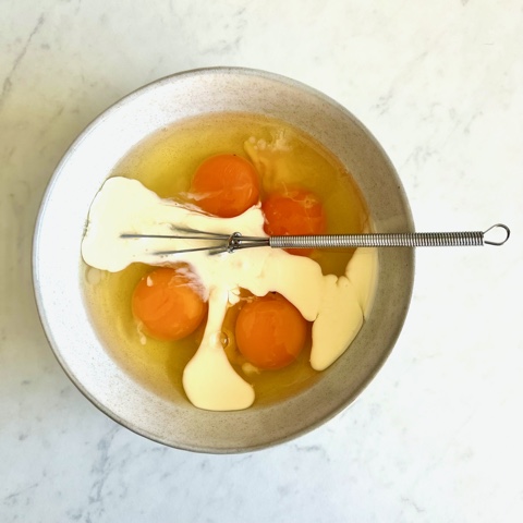 eggs and cream in a bowl with a small wire whisk
