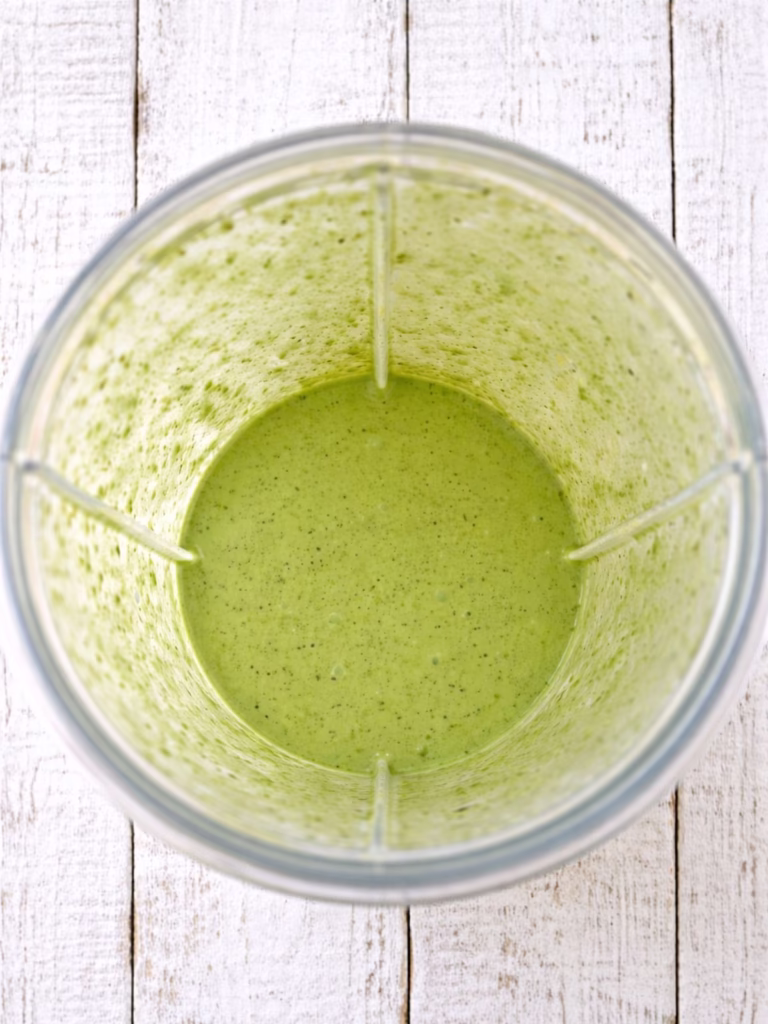 Green sauce blended in a clear blender jug, photographed overhead on a white timber background in natural light.