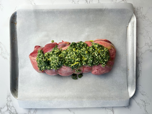 Boneless leg of rolled lamb on baking tray with baking paper and Greek marinade spooned over it