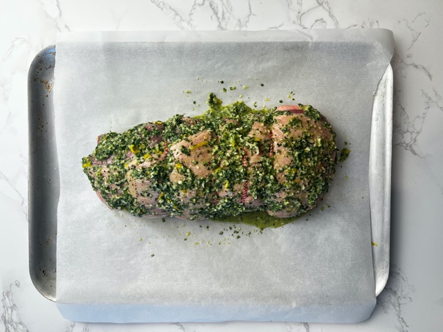 Boneless leg of rolled lamb on paper lined baking tray coated in a green marinade