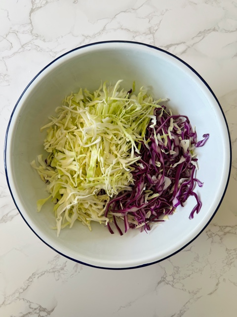 shredded cabbage in a white enamel bowl on marble bench