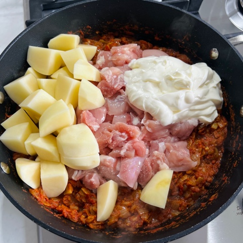 onion mixture in a pan with potatoes, chicken and yoghurt just added on top