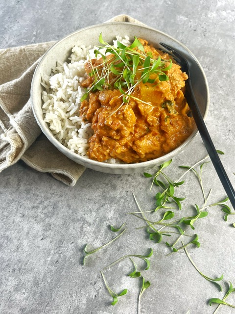 Chicken curry in a bowl with rice. Black Fork in it. Beige cloth on grey concret background. Coriander sprinkled around it