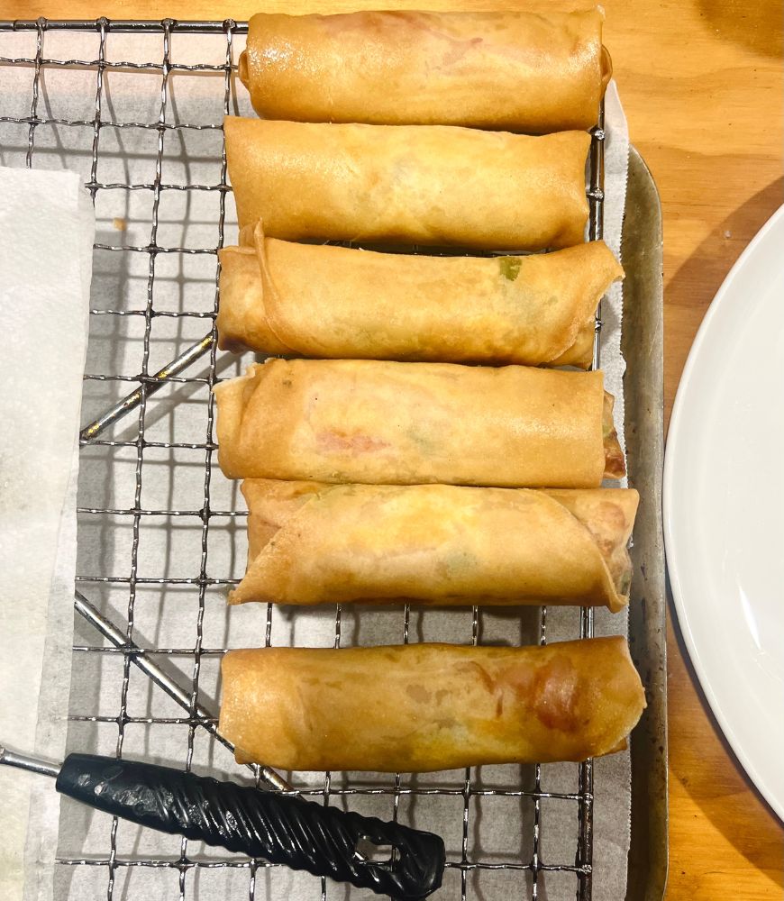 Deep fried chicken and ham spring rolls on a wire rack cooling