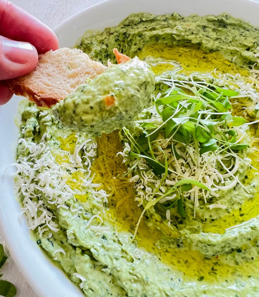 person scooping creamy fresh spinach dip in a white bowl  with a bread cracker