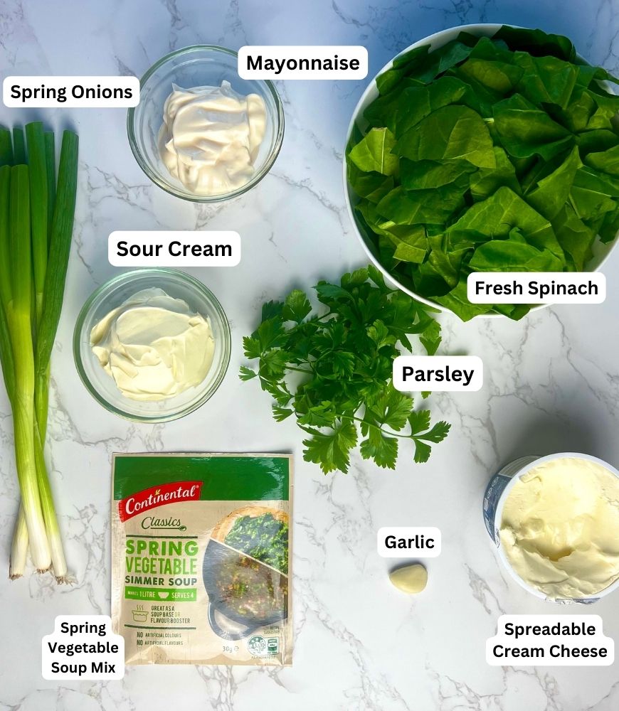 Fresh Spinach Dip ingredients laid out on a board. Spring onions, mayonnaise, sour cream, parsley, spinach, garlic, soup mix and cream cheese