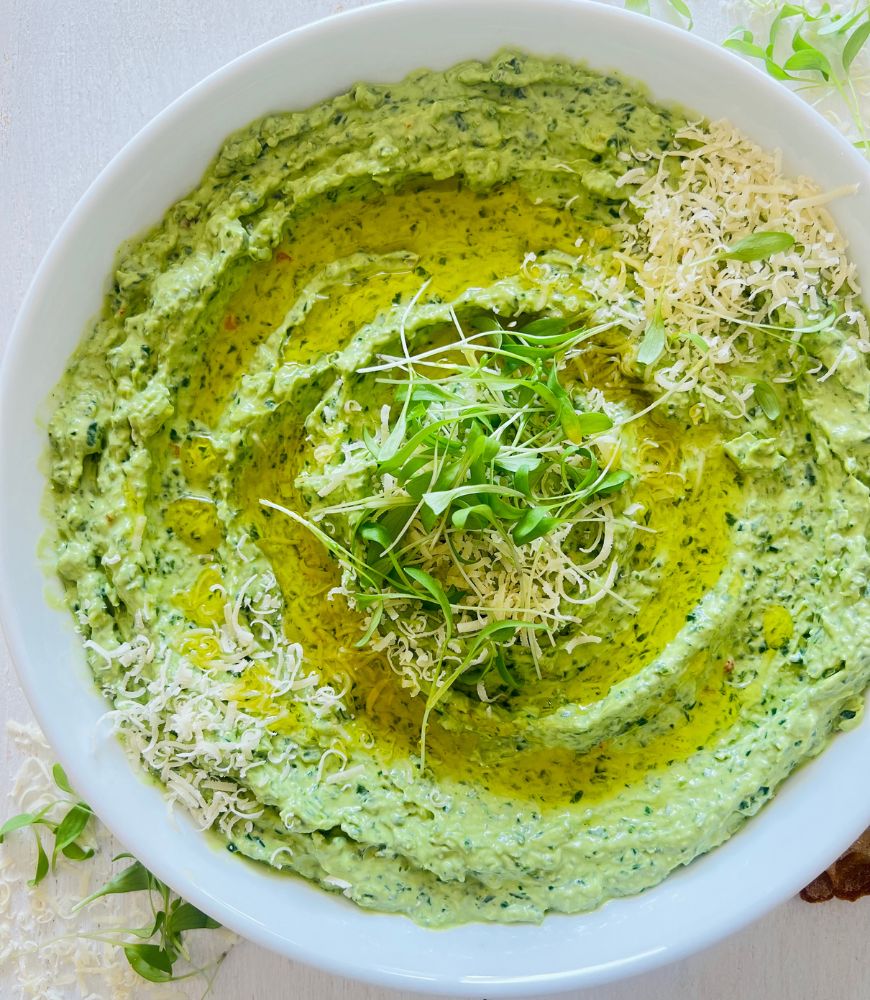 Creamy spinach dip in white bowl topped with grated parmesan, olive oil and microgreens