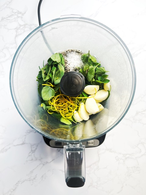 food processor with herbs, lemon and garlic in it