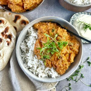 Indian Chicken Curry with Potato in a bowl with basmati rice and naan bread with yoghurt on the side