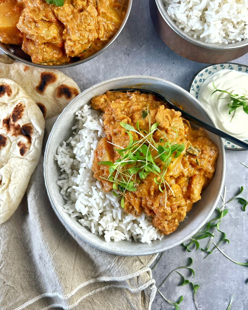 Indian chicken curry and rice in a grey bowl with black fork on grey background with naan bread 