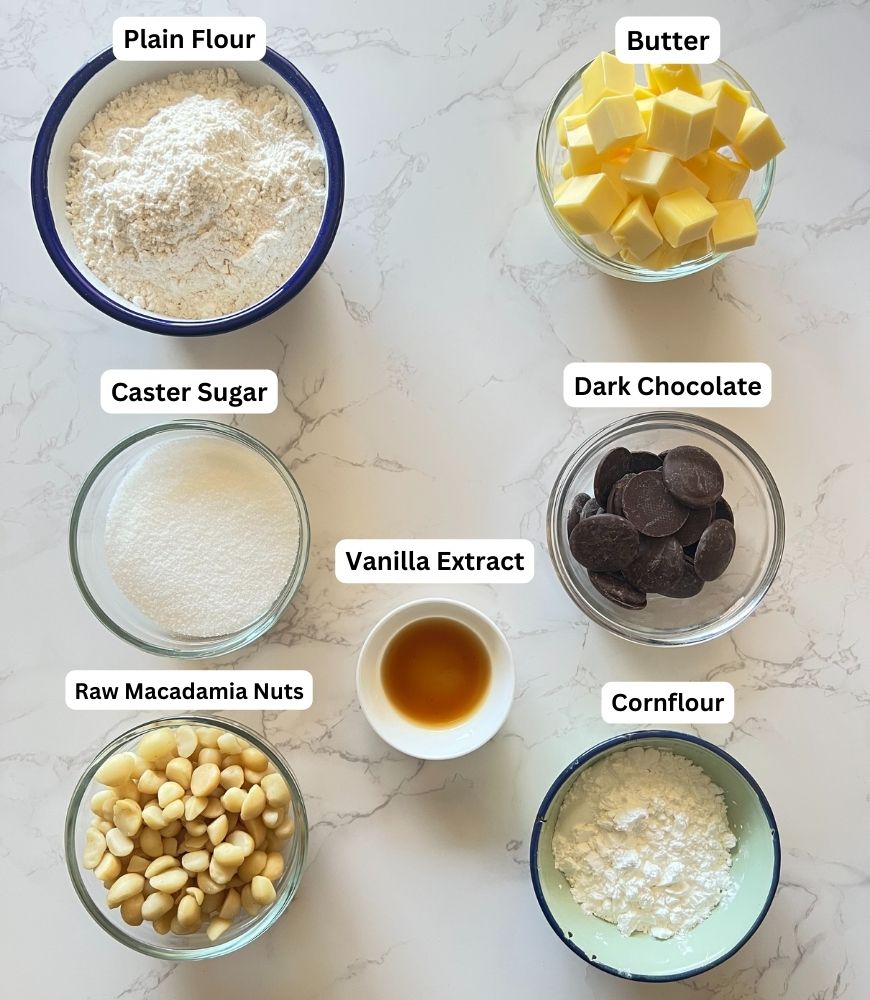 Macadamia Nut Shortbread ingredients laid out in small bowls on marble background.
Plain flour, butter, sugar, macadamia nuts, cornflour, vanilla extract and dark chocolate