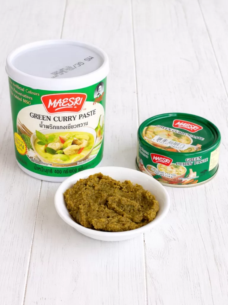 Maesri green curry paste displayed in a large 400g tub and small 114g can, with a bowl of the curry paste in front on a white surface.