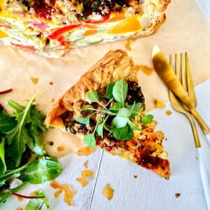 ROAST VEGETABLE QUICHE WITH FILLO WEDGE WITH KNIFE AND FORK ON BAKING PAPER AND WHITE BACKGROUND