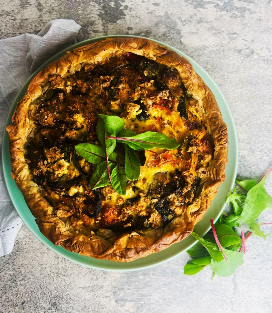 Overhead image of quiche on a green plate with salad leaves.