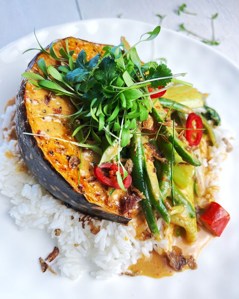 Bed of rice on a white plate topped with baked pumpkin, beans, chilli, coriander and red curry sauce