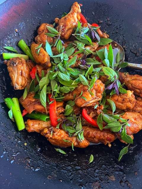 Thai basil chicken wings in wok with Thai basil over the top