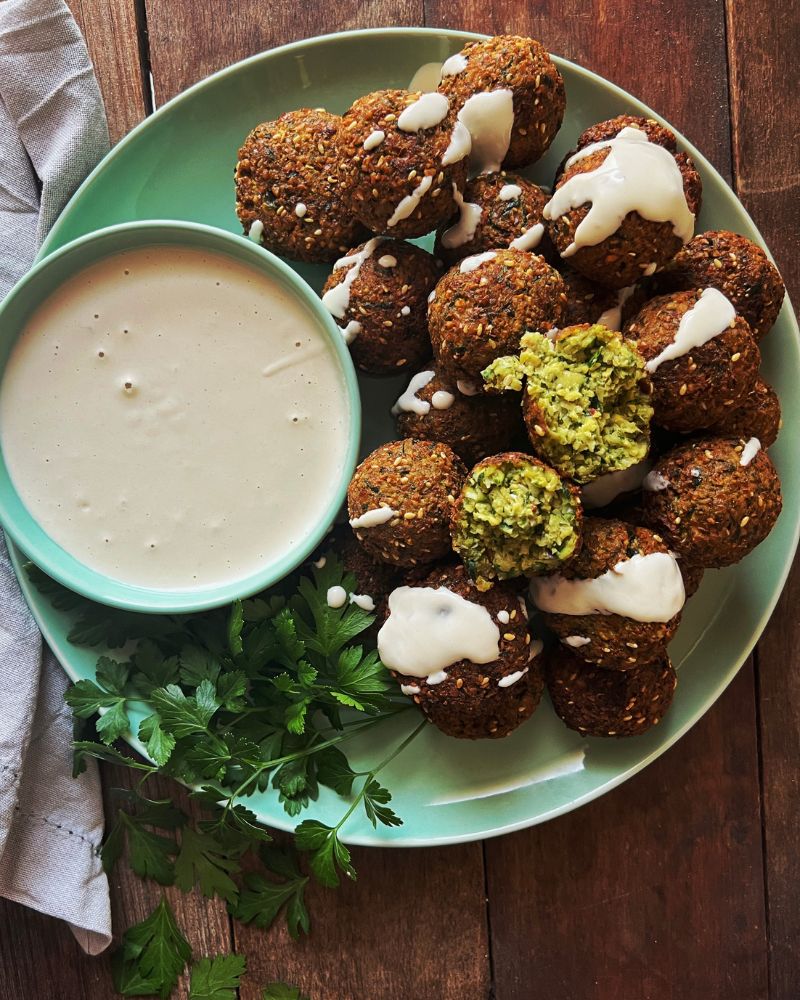 Zucchini & Sesame Falafels on a green plate with a bowl of tahini dipping sauce and some parsely as garnish. Set on a wooden background